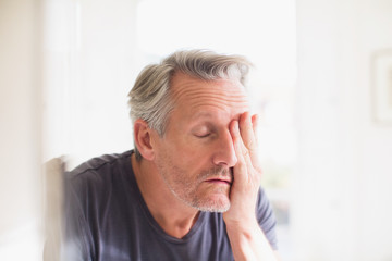 Tired mature man with head in hand at bathroom mirror