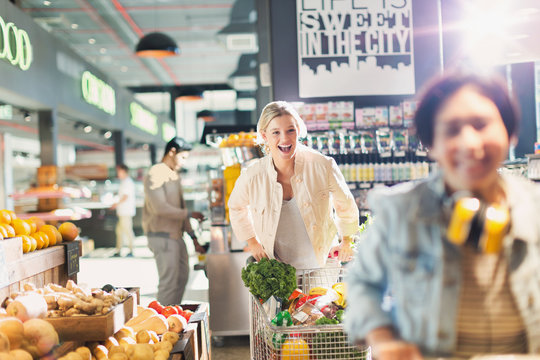 Playful young woman laughing, pushing shopping cart in grocery store market