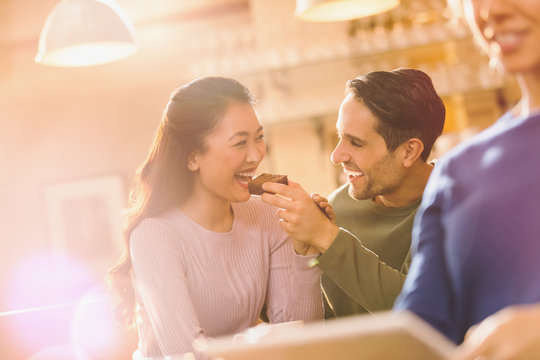 Playful boyfriend feeding brownie to girlfriend at cafe