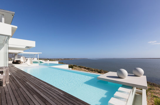 Sunny, tranquil modern luxury home showcase exterior infinity pool with ocean view under blue sky