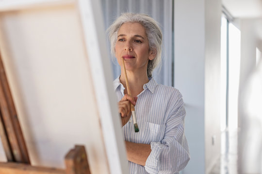 Pensive mature woman painting at easel