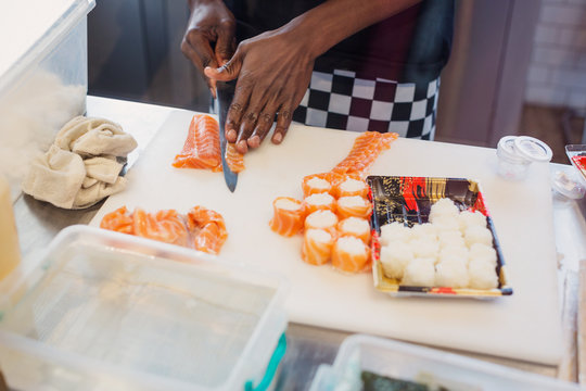 Young female chef slicing salmon, making sushi in restaurant