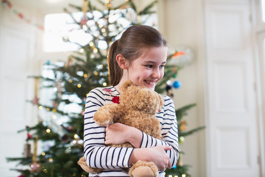 Happy girl hugging teddy bear in front of Christmas tree