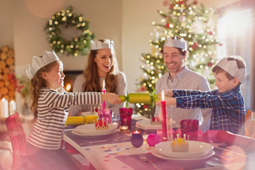 Family in paper crowns pulling Christmas cracker at dining table