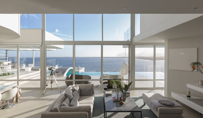 Sunny, tranquil modern luxury home showcase interior living room with patio and ocean view
