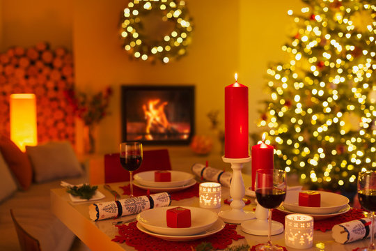 Ambient candles and Christmas crackers on dinner table in living room with fireplace and Christmas tree