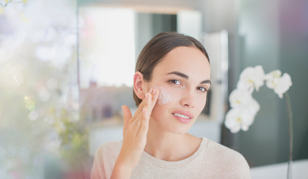Portrait brunette woman applying face moisturizer to cheek