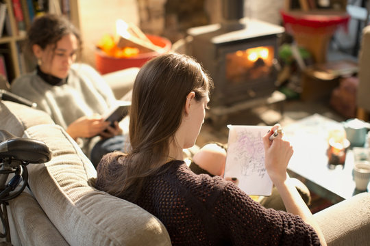 Young woman drawing, sketching in notepad in living room