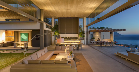 Illuminated modern, luxury home showcase interior living room open to patio at dusk