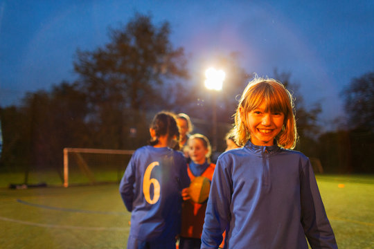 Portrait confident girl playing soccer with team on field at night