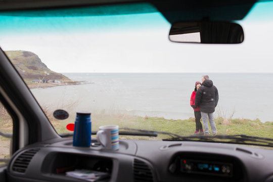 Couple talking outside motor home on cliff overlooking ocean