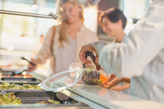 Young woman serving salad at salad bar in grocery store market