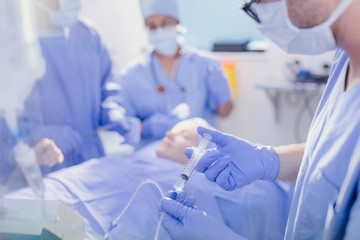 Anesthesiologist with syringe injecting anesthesia into IV drip in operating room