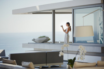 Woman with digital camera photographing ocean view on modern, luxury home showcase balcony