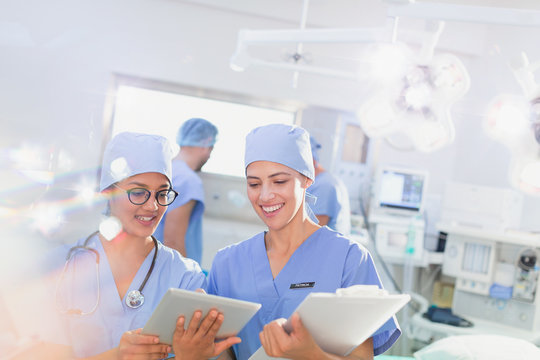 Smiling female surgeons using digital tablet and clipboard in operating room - Powered by Adobe