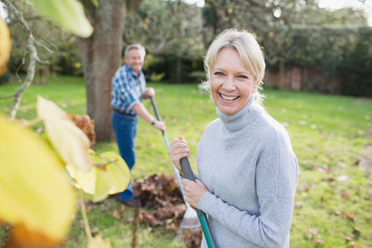 Portrait smiling, confident mature woman raking autumn leaves in backyard