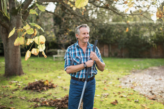 Smiling senior man raking autumn leaves in backyard
