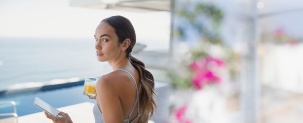 Brunette woman drinking orange juice and using digital tablet on luxury patio