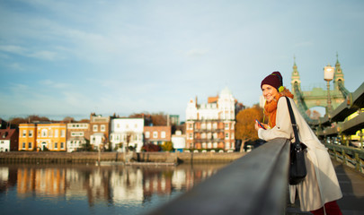 Young woman in stocking cap and scarf on urban autumn bridge