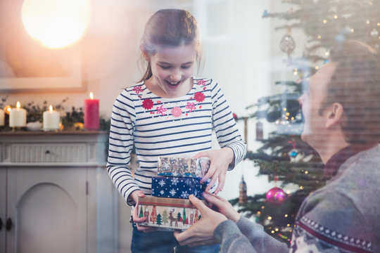 Daughter giving stack of Christmas gifts to father in living room