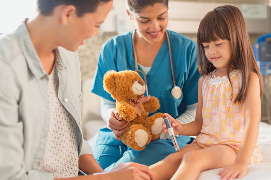 Naklejki Female nurse with teddy bear watching girl patient using insulin pen in hospital room