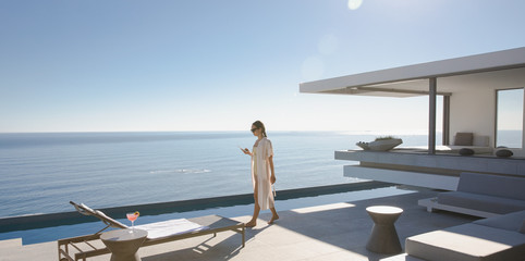 Woman walking on sunny, modern, luxury home showcase exterior patio with ocean view