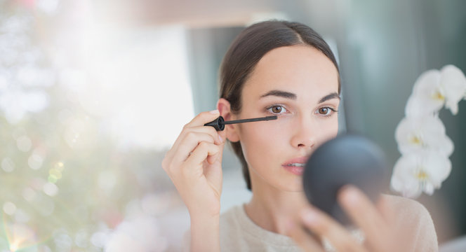 Woman apply mascara with mascara wand and compact mirror