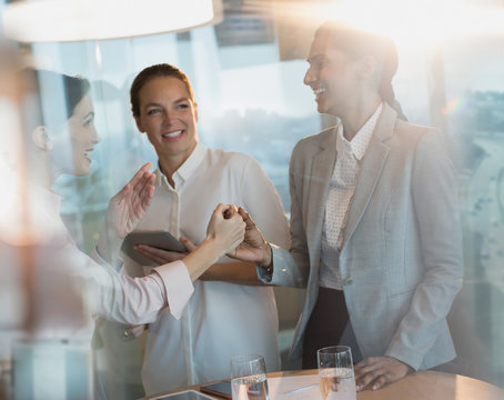 Businesswomen laughing, handshaking in office meeting