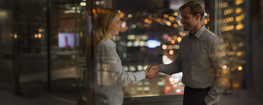 Businessman and businesswoman handshaking in office at night