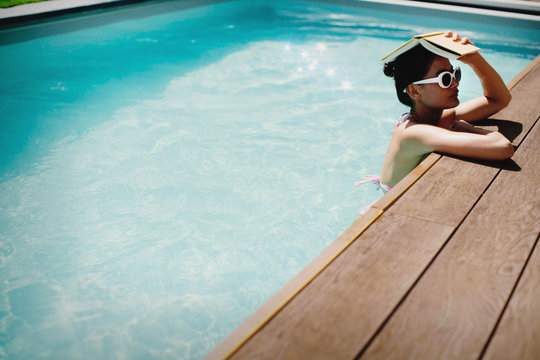 Woman holding book overhead in sunny summer swimming pool