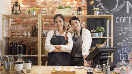 Portrait of two asian women baristas in aprons in cozy coffee shop. Young female employees in...