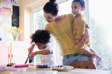 Mother helping toddler daughter cutting breakfast waffles