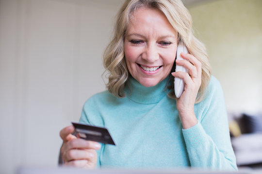 Smiling mature woman with credit card talking on telephone