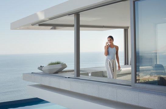 Woman talking on cell phone on modern, luxury home showcase exterior patio with ocean view