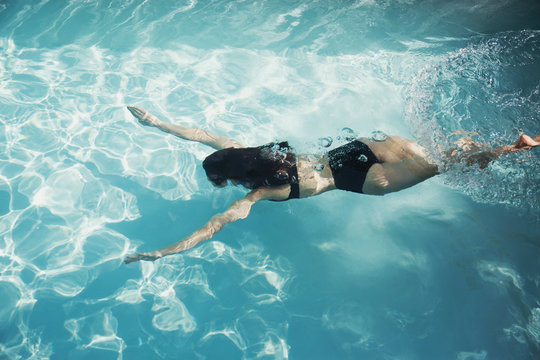 Woman in bikini swimming underwater in sunny swimming pool