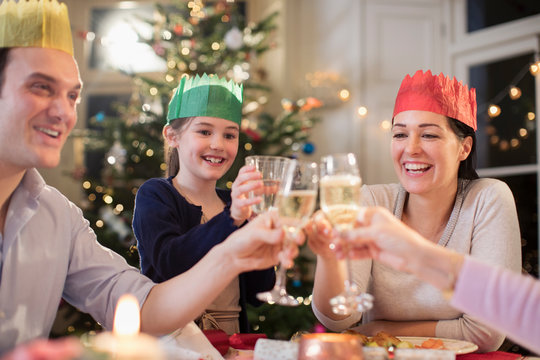 Happy family in paper crows toasting water and champagne glasses at Christmas dinner