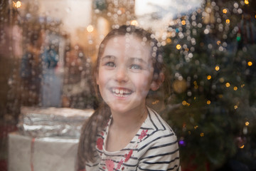 Portrait happy girl at wet window in Christmas living room