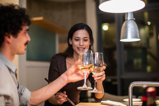 Couple toasting white wine glasses in apartment kitchen