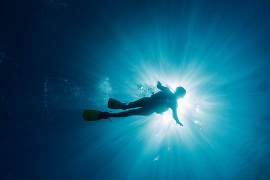 Sun shining behind woman scuba diving underwater, Maldives, Indian Ocean