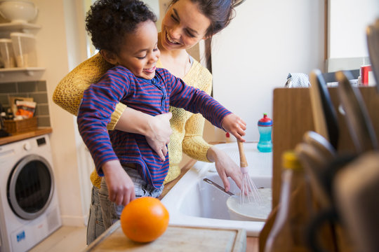 Happy mother and toddler son doing dishes at kitchen sink