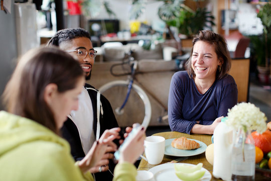 Young adult roommate friends enjoying breakfast at apartment kitchen table