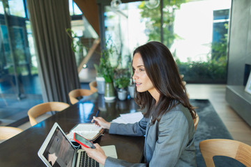 Businesswoman working from home, using smart phone and laptop