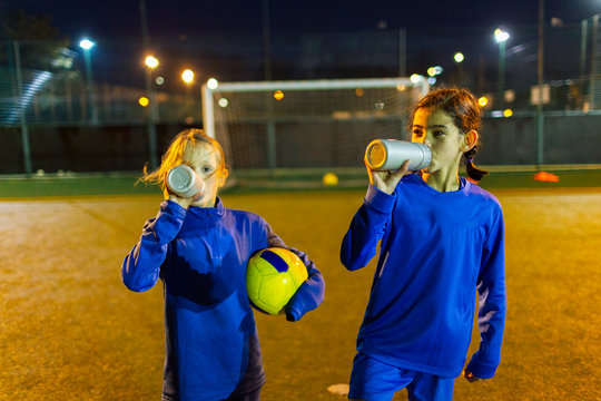 Girl soccer players taking a break, drinking water on field at night