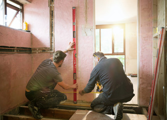 Construction workers using level too and tape measure in house