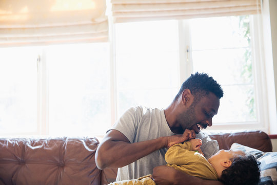 Playful, affectionate father and son cuddling on living room sofa