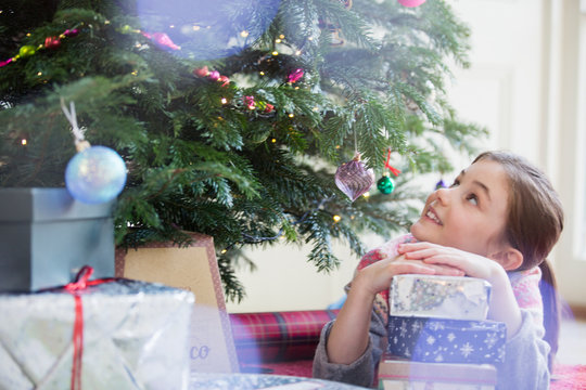 Curious girl with stack of gifts looking up at Christmas tree