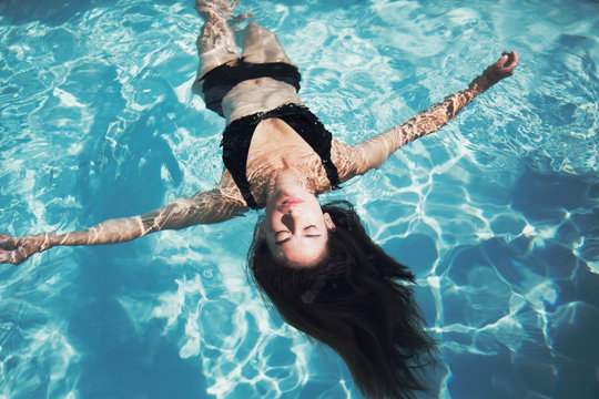 Serene woman in black bikini floating in sunny summer swimming pool