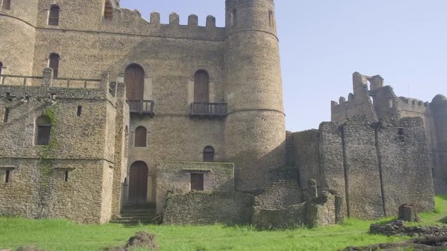 Camera tracking right low angle view past Fasilides Castle southern facade to reveal distant view of Palace of Iyasu I ruins in Gondar, Ethiopia