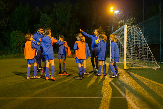 Girls Soccer Team Listening To Coach On Field At Night