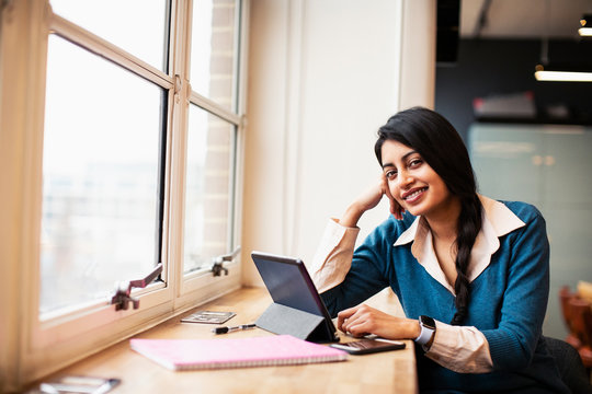 Portrait confident, smiling businesswoman using digital tablet in window